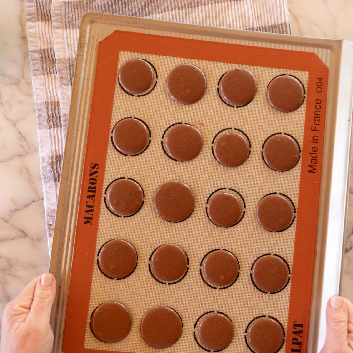 Tapping the tray of piped macaron batter, to release air bubbles.
