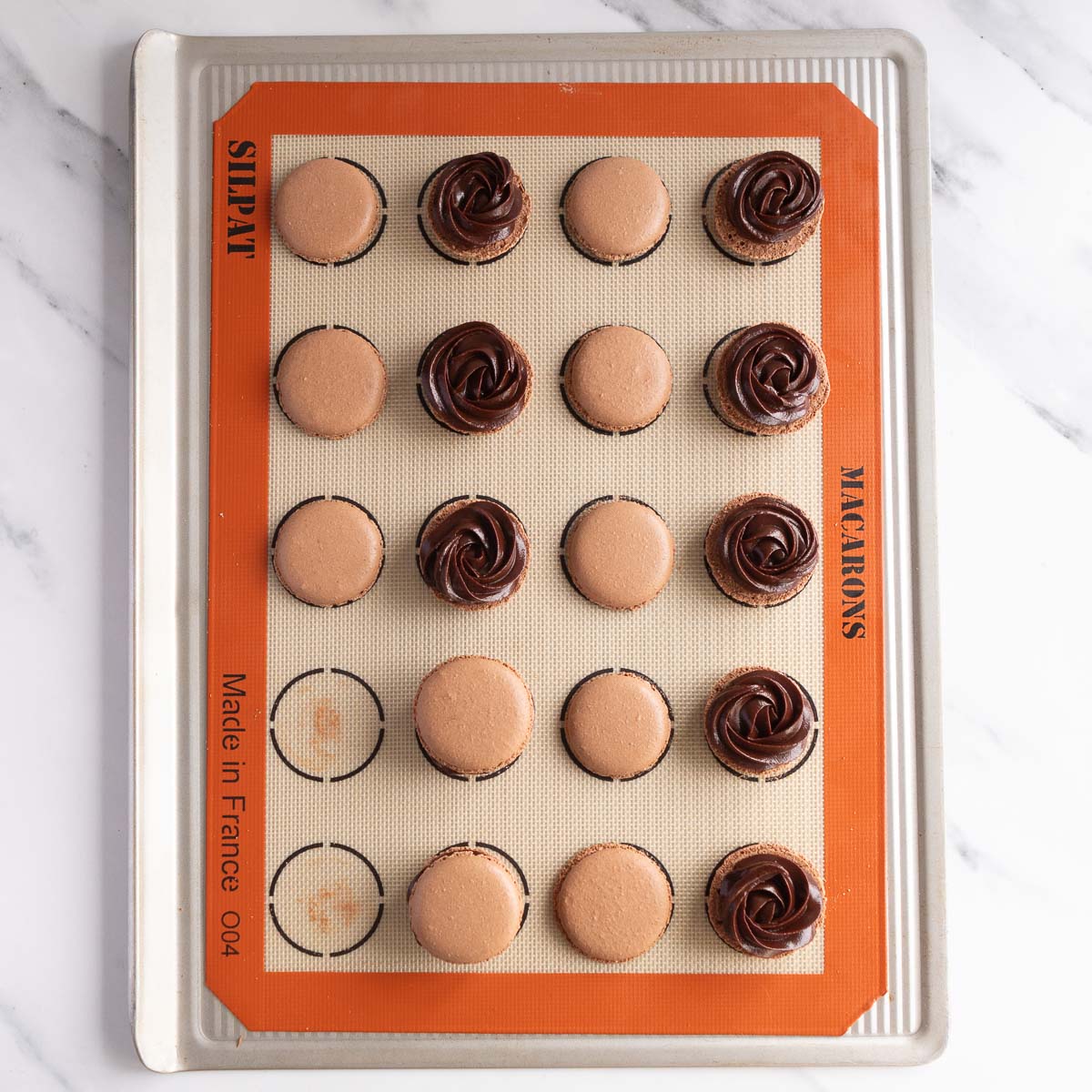 Chocolate ganache is piped onto half of the shells, then topped with the remaining half of the shells.