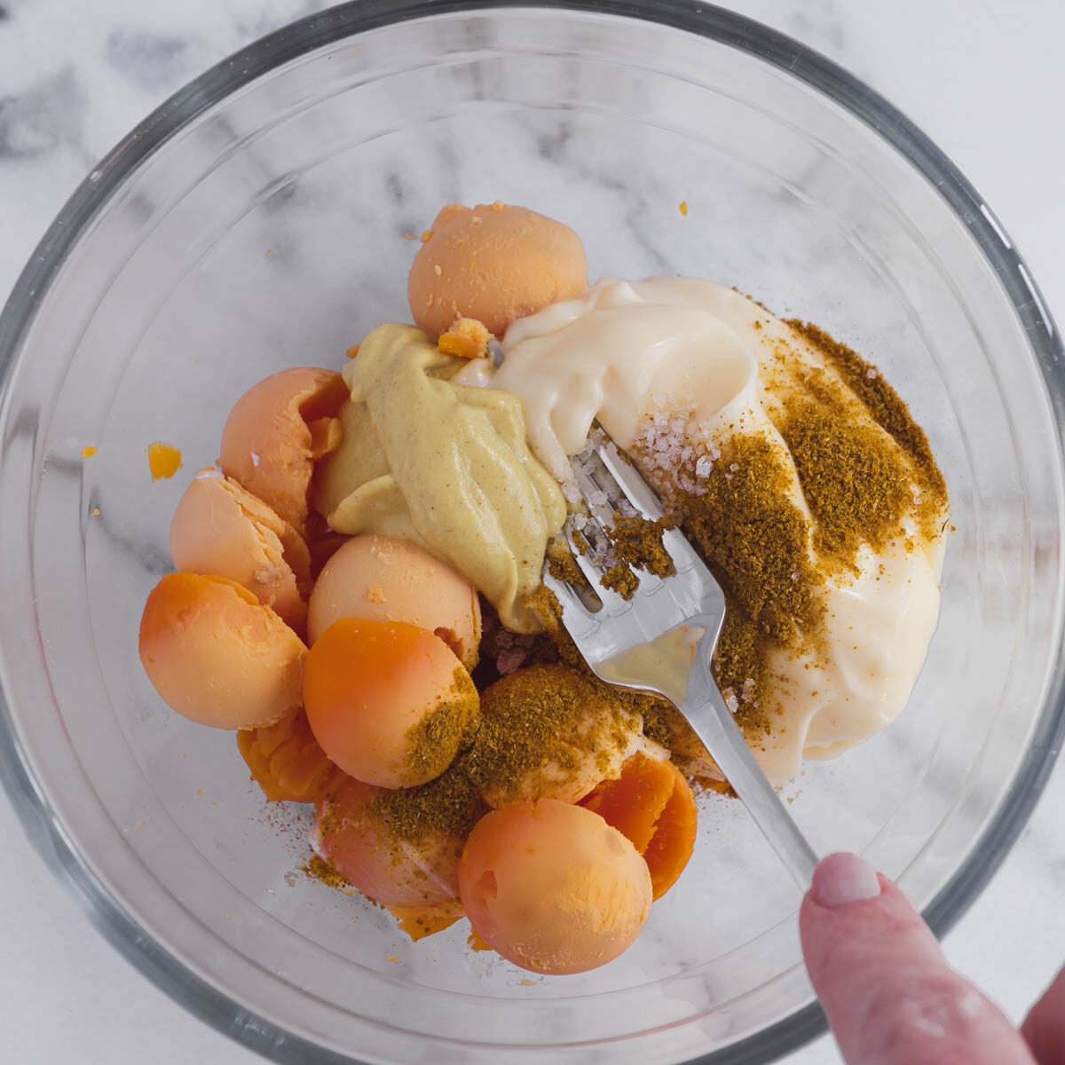 Masing yolks with mayonnaise, mustard, curry and salt to make the filling for curried devilled eggs.