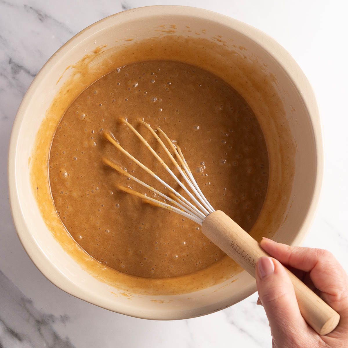 Adding the dry ingredients of a gingerbread bundt cake to the wet ingredients.