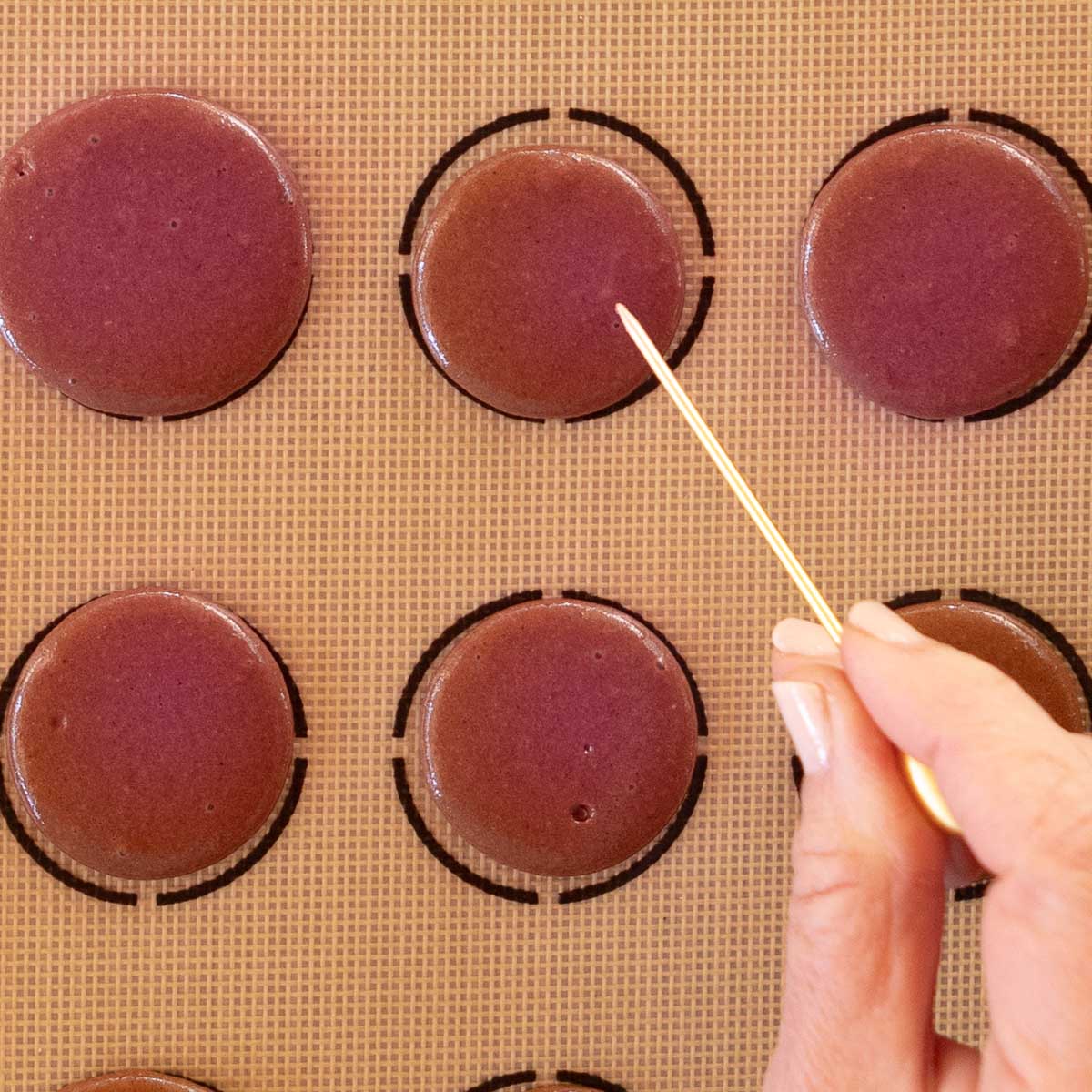 Use a toothpick to remove air bubbles from macaron shells.