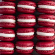 Rows of colourful red velvet macarons, filled with cream cheese frosting.