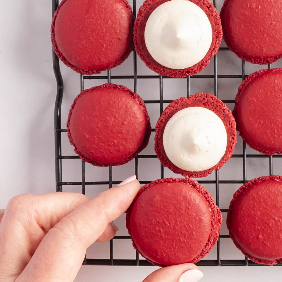 Filling red velvet macaron shells with cream cheese frosting.