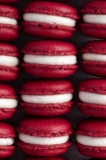 Rows of colourful red velvet macarons, filled with cream cheese frosting.