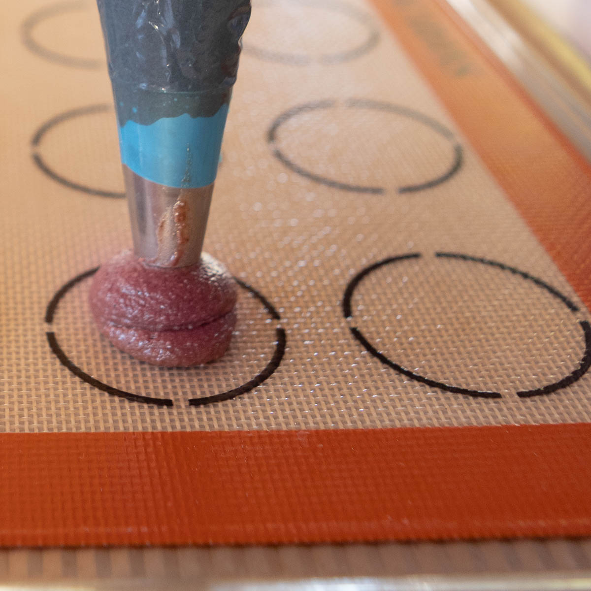 Piping red velvet macaron shells onto a silpat mat.