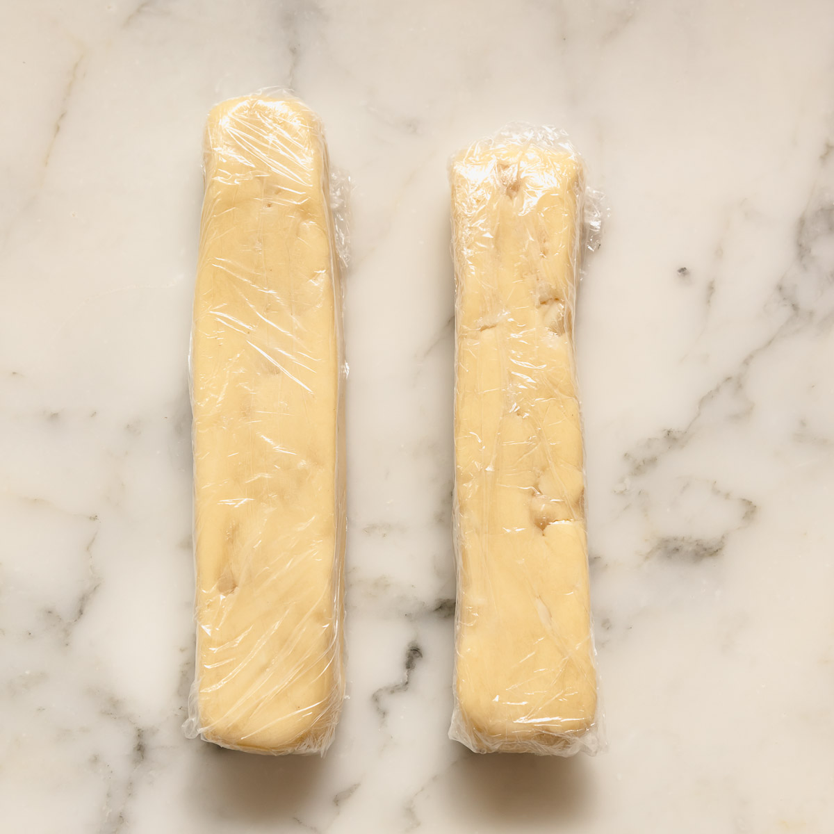 Rolling shortbread dough into a log and wrapping it in plastic wrap, before chilling.